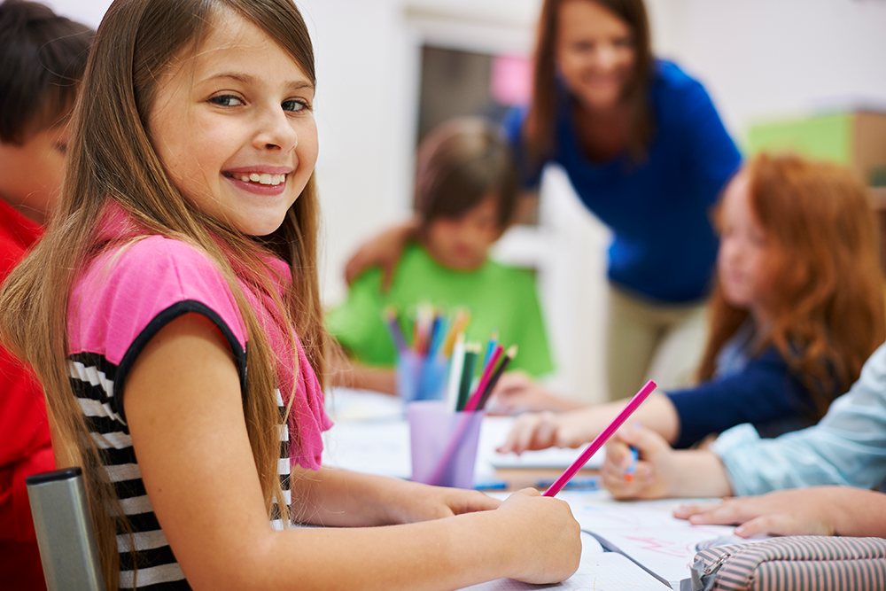 Aluna do ensino fundamental sentada ao lado de outros alunos enquanto conversam com a professora.