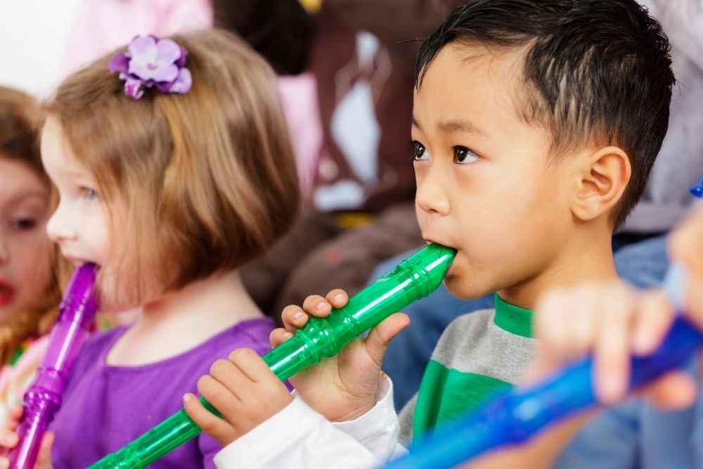 Grupo de crianças tocando flauta, com destaque para um menino com uma flauta verde.