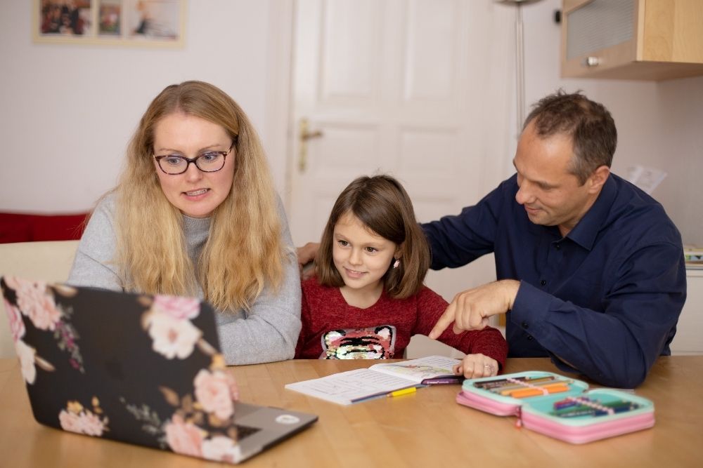 Uma mulher, uma menina e um homem sentados em uma mesa olhando para a tela de um computador.