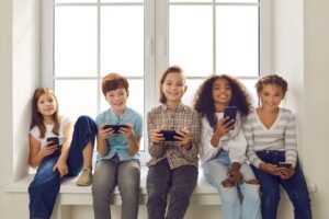 Grupo de crianças sentadas e sorrindo, com celulares nas mãos.