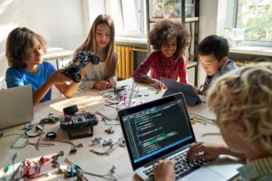 grupo de estudantes diversos manuseiam peças eletrônicas e notebook.